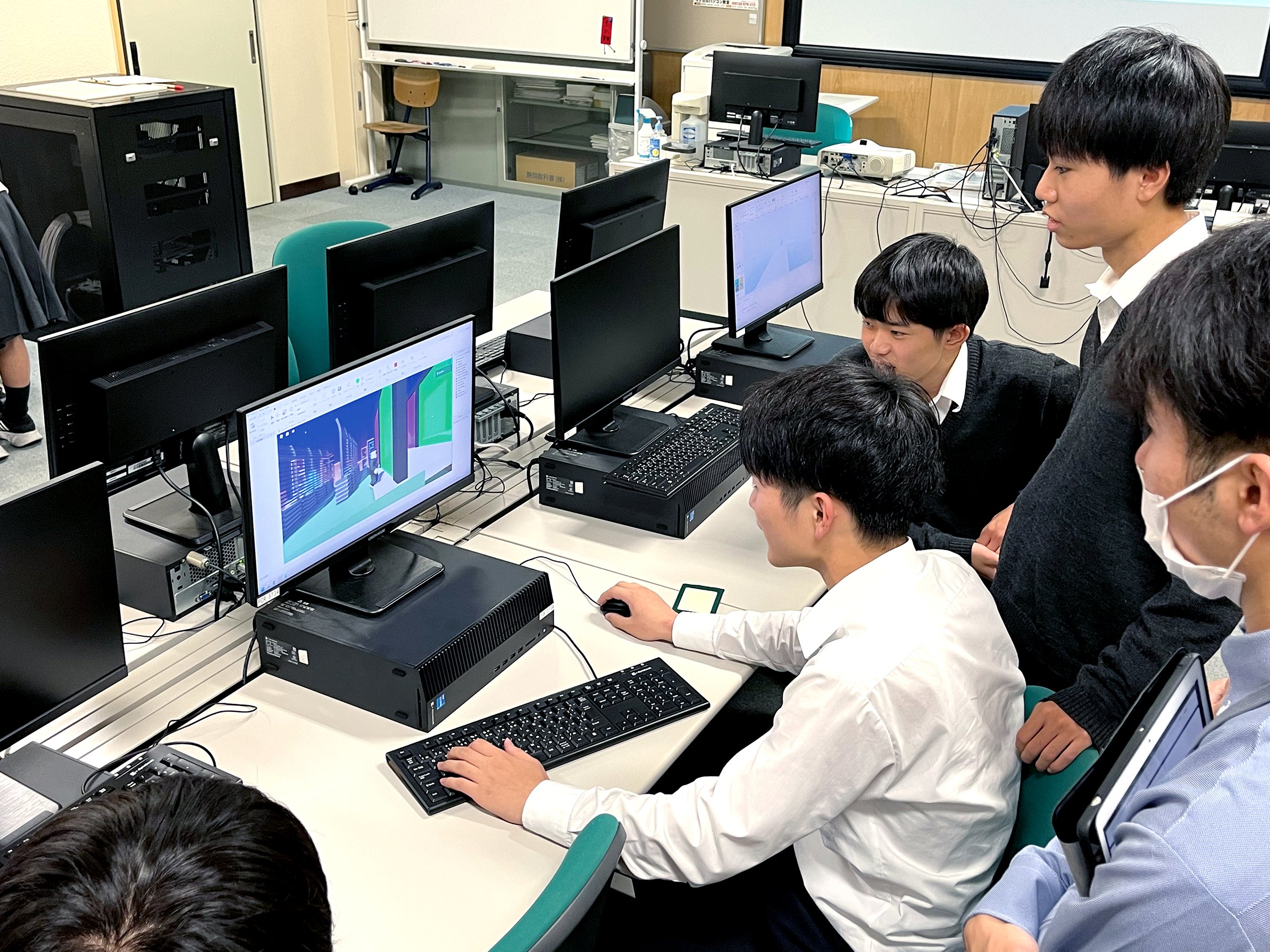 プログラミングをする男子生徒と、それを見守る学友の写真